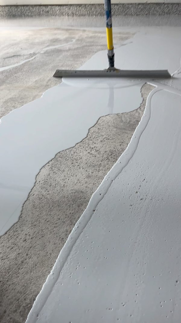 Gray epoxy base coat being squeegeed across a garage floor