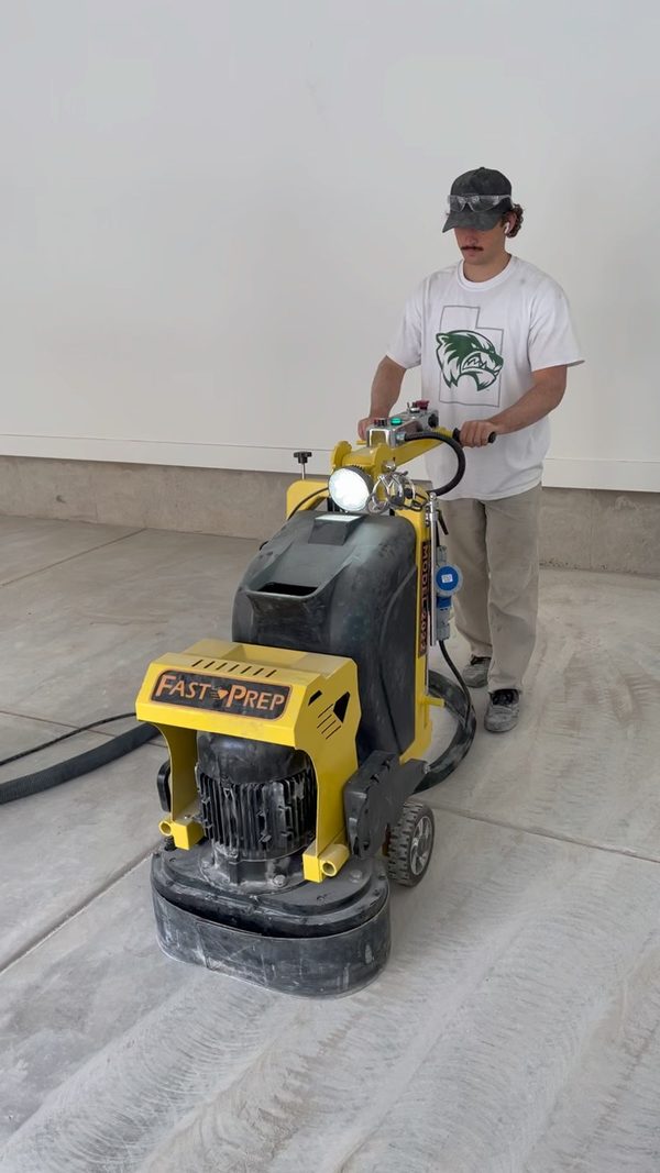 Crew member grinding a bare concrete garage floor with a diamond grinder