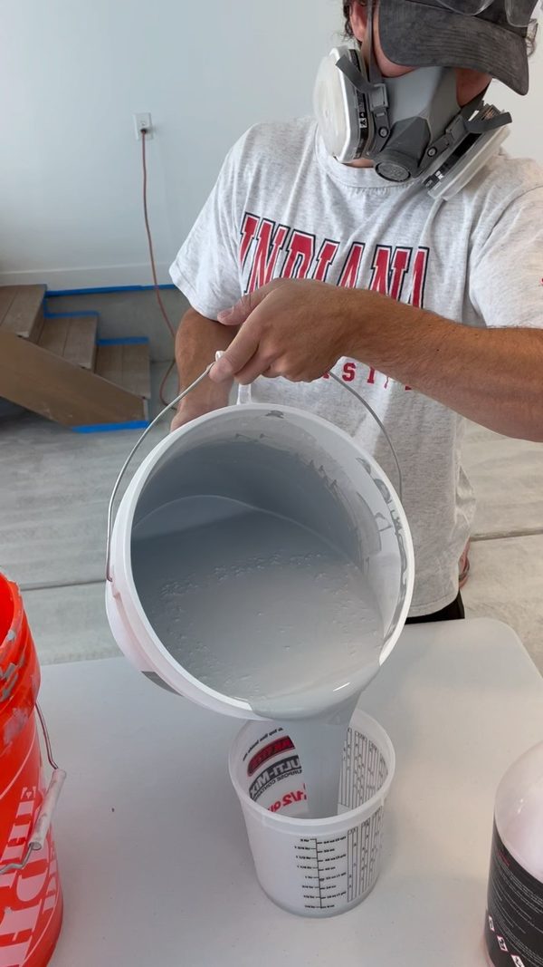Crew member pouring mixed gray epoxy into a measuring cup